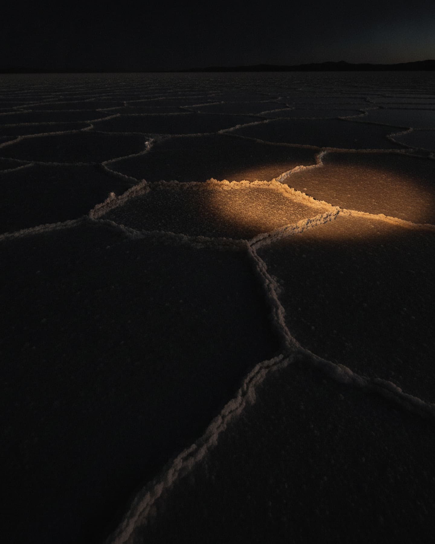 Weite Salzfläche im Dämmerlicht, von einem einzelnen warmen Lichtstreifen am Horizont getroffen
